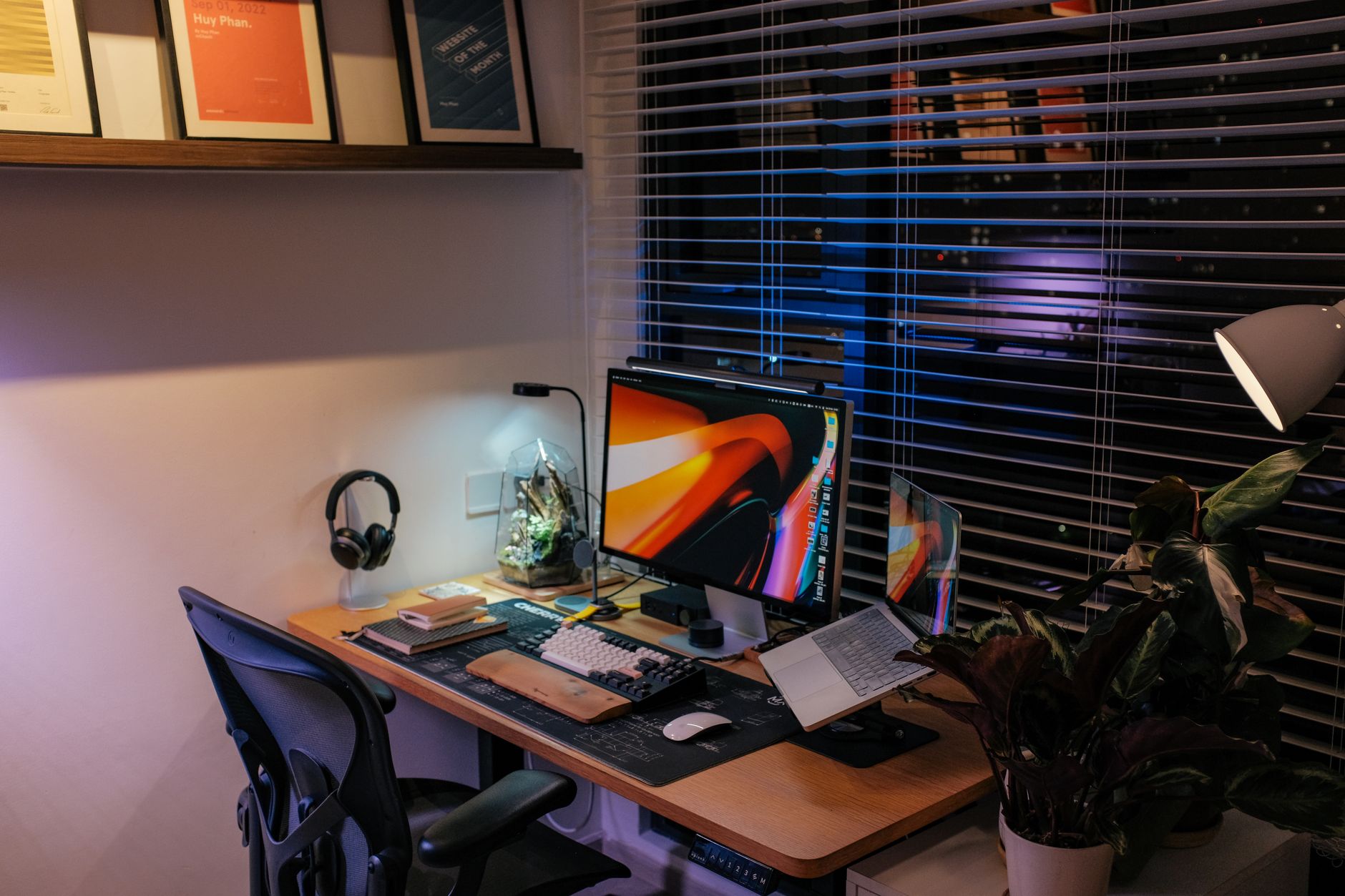 Bureau à domicile confortable avec ordinateur et éclairage ambiant, plantes vertes en arrière-plan.